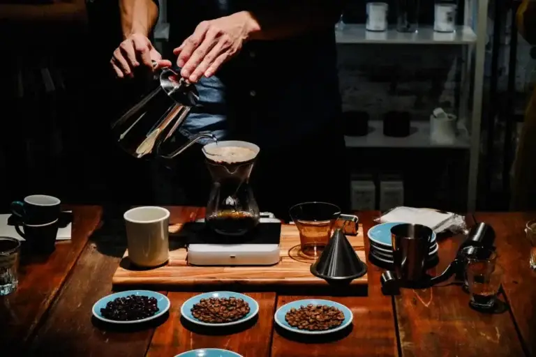 Barista preparing pour-over coffee with beans and brewing tools on a wooden table