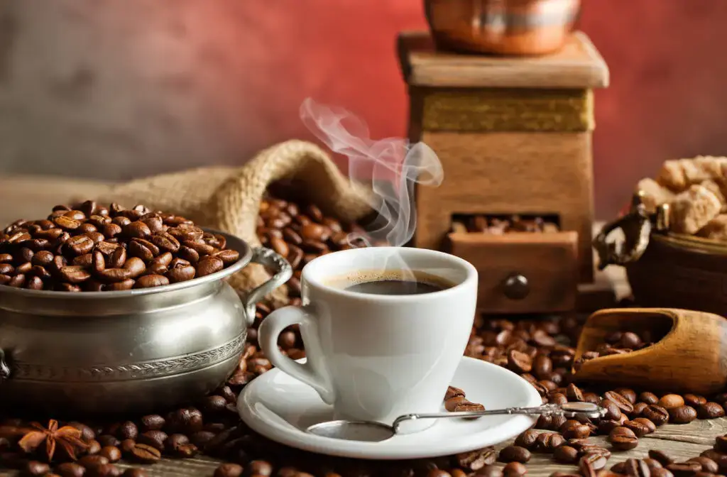 Steaming cup of coffee surrounded by roasted beans and rustic accessories