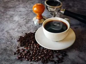 Fresh espresso in a white cup with coffee beans, grounds and a barista tamper